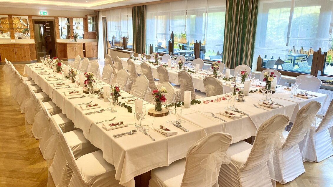 Ein eleganter Speisesaal mit einem langen, festlich gedeckten Tisch. Die Stühle sind mit weißen Überzügen dekoriert und mit Blumen geschmückt. | © Gasthof Landhotel Hubmann