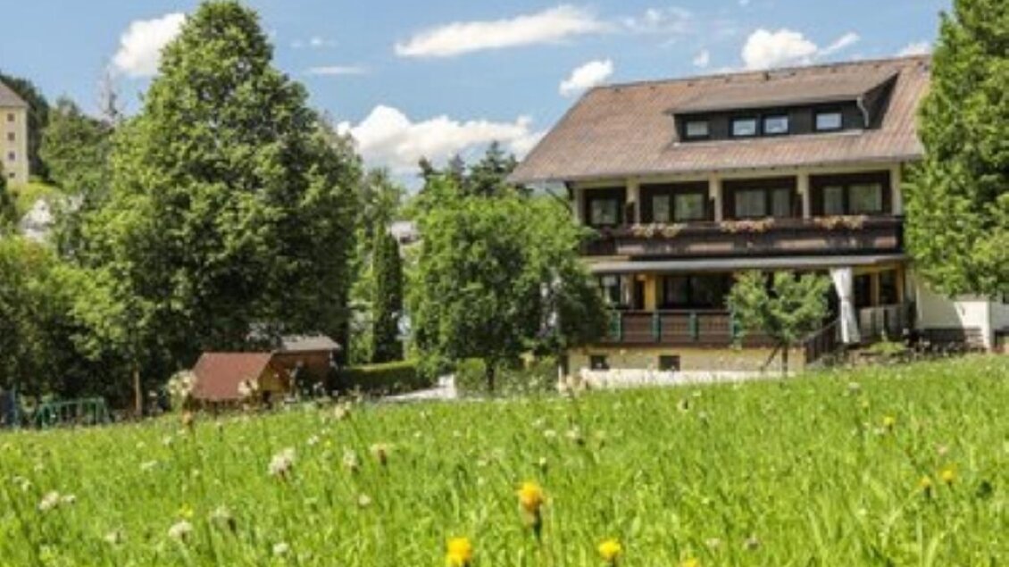 Gasthof Leitner mit Balkon und großem Garten in blühender Wiese unter blauem Himmel. | © Gasthof Leitner