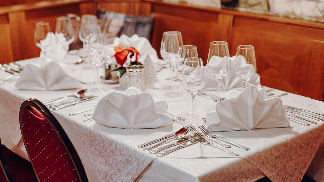 Ein eleganter Tisch mit schön gefalteten Servietten und Gläsern. Die Tischdecke ist hell und es gibt dekorative Elemente in der Mitte. | © Gasthof Lobmingerhof
