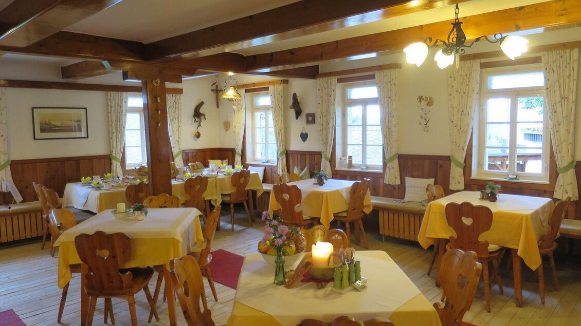 Ein einladendes Restaurant mit Tischen, die mit gelben Tischdecken gedeckt sind. Die Wände sind mit Dekorationen geschmückt und große Fenster sorgen für viel Tageslicht. | © Gasthof Mörth