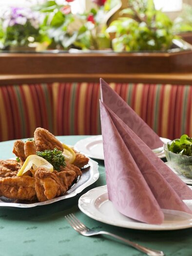Ein schön gedeckter Tisch mit lila Servietten. Auf dem Teller liegt ein leckerer Hühnerbraten mit Beilagen. | © Stephan Friesinger