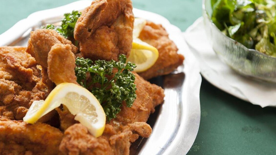 Ein Teller mit knusprig gebratenem Hähnchen, garniert mit Zitronenscheiben und Petersilie. Neben dem Hähnchen befindet sich eine Schüssel mit frischem Salat. | © Stephan Friesinger