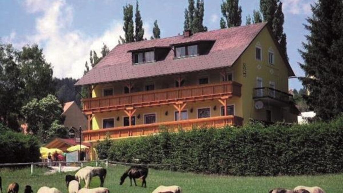 Lipizzanerpferde grasen auf einer Wiese in Piber, vor ländlicher Kulisse mit Bäumen und dem Gasthof Piberwirt.  | © Günter Bardel