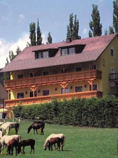 Lipizzanerpferde grasen auf einer Wiese in Piber, vor ländlicher Kulisse mit Bäumen und dem Gasthof Piberwirt.  | © Günter Bardel