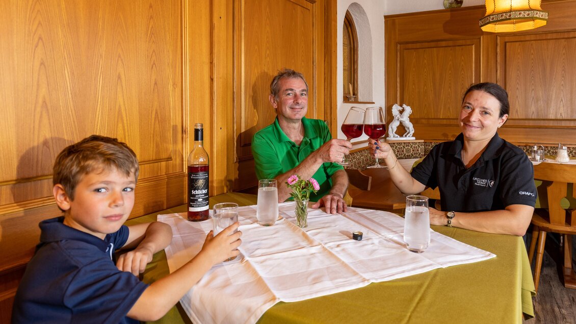 Gastgeberfamilie sitzt mit Kind im traditionellen Gasthof Piberwirt und stößt am gedeckten Tisch im Holzinterieur an. | © Lipizzanerheimat | Harry Schiffer