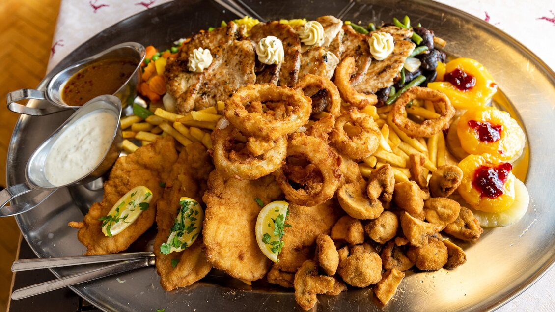 Großer Teller mit einer Vielzahl an frittierter Speisen, darunter Schnitzel, Zwiebelringe, Pommes und Gemüse, begleitet von Saucen und Garnierungen im Gasthof Reinisch in Köflach. 
 | © TV Region Graz - Harry Schiffer