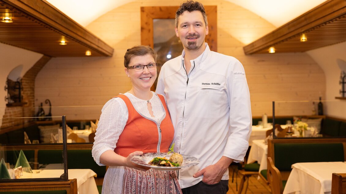 Ein freundliches Team in einem Restaurant steht zusammen. Die Frau trägt ein traditionelles Outfit und hält einen Teller mit Essen. | © 5komma5sinne