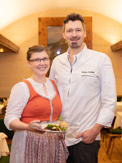 A friendly team in a restaurant stands together. The woman wears a traditional outfit and holds a plate with food. | © 5komma5sinne