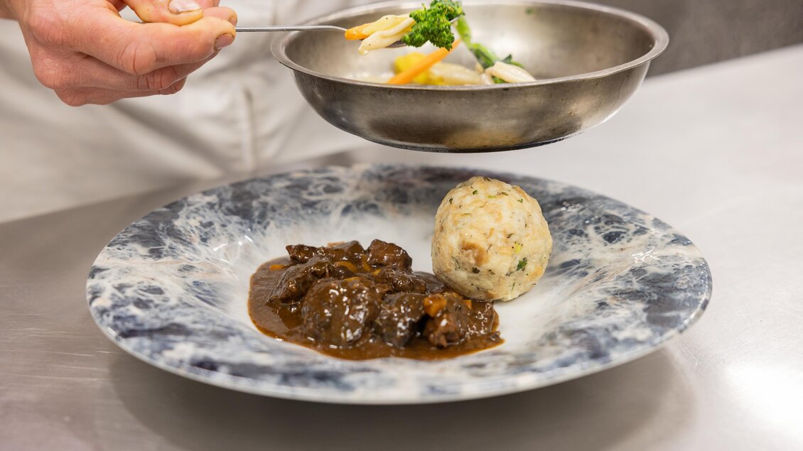 Ein Teller mit einem saftigen Fleischgericht, einer Beilage aus Knödeln und Gemüse. Die Präsentation ist ansprechend und appetitlich. | © 5komma5sinne