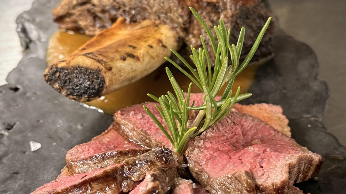 Eine köstliche Fleischplatte mit saftigem Rindersteak und einer gebratenen Knochenhälfte. Mit frischem Rosmarin garniert, appetitlich präsentiert auf einem dunklen Stein. | © Seetalblick