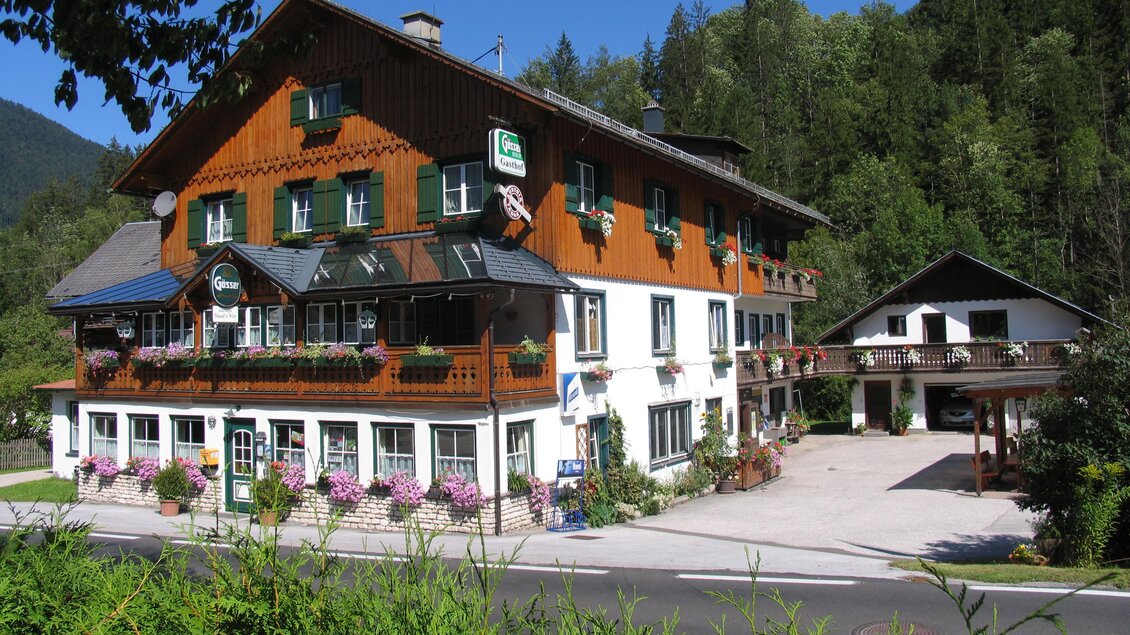Ein charmantes Alpenhaus mit Holzverkleidung und Balkonen. Umgeben von grünen Bäumen und blühenden Blumen. | © Gasthof Staudnwirt