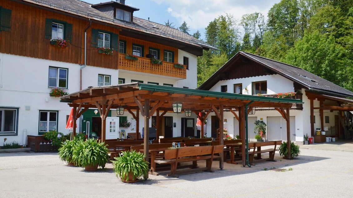 Ein traditionelles Landhaus mit Holzverkleidung und Blumenkästen. Im Vordergrund befindet sich eine überdachte Terrasse mit Sitzgelegenheiten. | © Gasthof Staud'nwirt