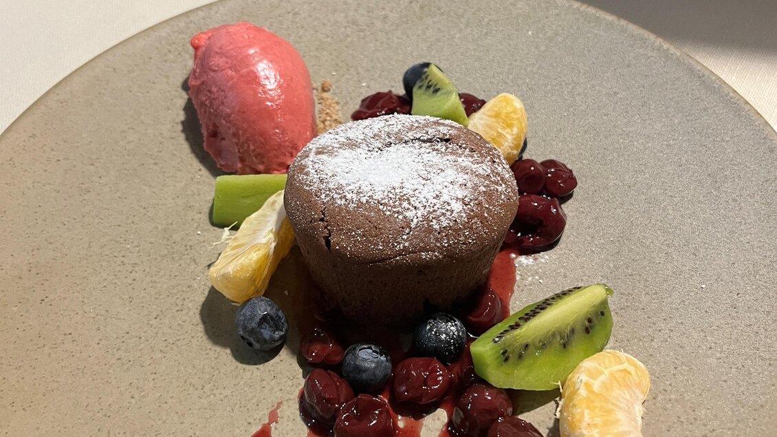 Ein leckeres Dessert auf einem weißen Teller. Es besteht aus einem Schokoladenkuchen, Sorbet und frischen Früchten.