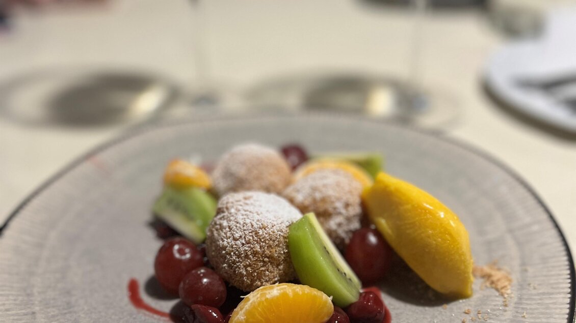 Ein kunstvoll angerichtetes Dessert auf einem weißen Teller. Es besteht aus Fruchtstücken und kleinen, mit Puderzucker bestäubten Köstlichkeiten. | © Alexandra Wippel