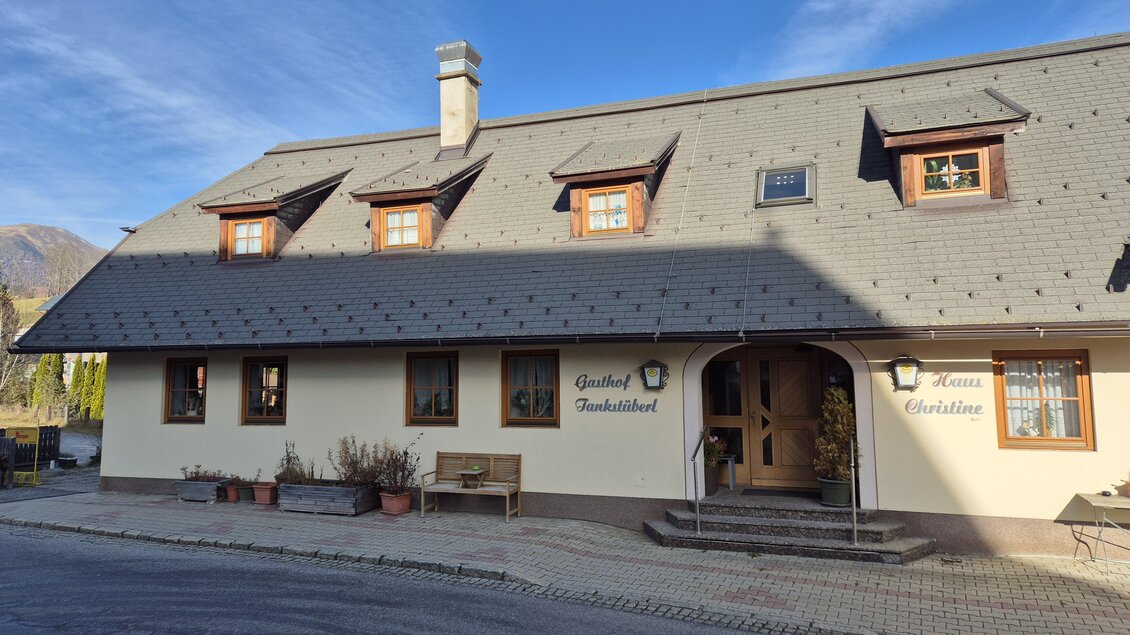 Ein charmantes Gasthaus mit einem traditionellen Dach und Holzfenstern. Es liegt in einer ländlichen Umgebung und ist von einer ruhigen Straße umgeben. | © Tourismusverband Murau