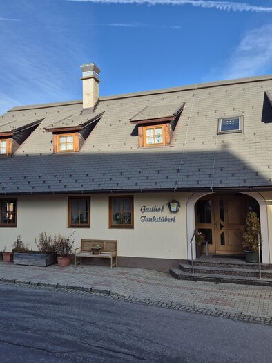 Ein charmantes Gasthaus mit einem traditionellen Dach und Holzfenstern. Es liegt in einer ländlichen Umgebung und ist von einer ruhigen Straße umgeben. | © Tourismusverband Murau