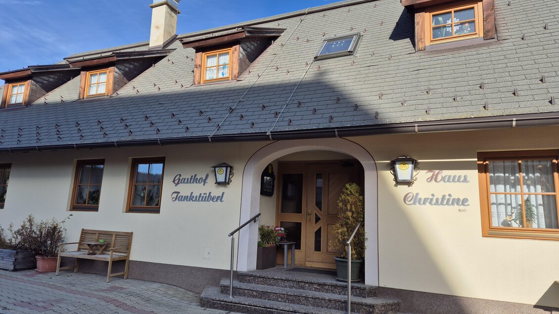 Ein gemütliches Gasthaus mit einem einladenden Eingang. Das Gebäude hat ein dunkles Dach und Holzfenster, umgeben von Pflanzen und Bänken. | © Tourismusverband Murau