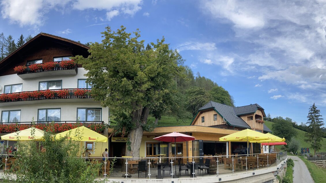 Ein charmantes Gasthaus mit mehreren Etagen und Balkonen. Im Freien stehen bunte Sonnenschirme für Gäste. | © Gasthof Trattner
