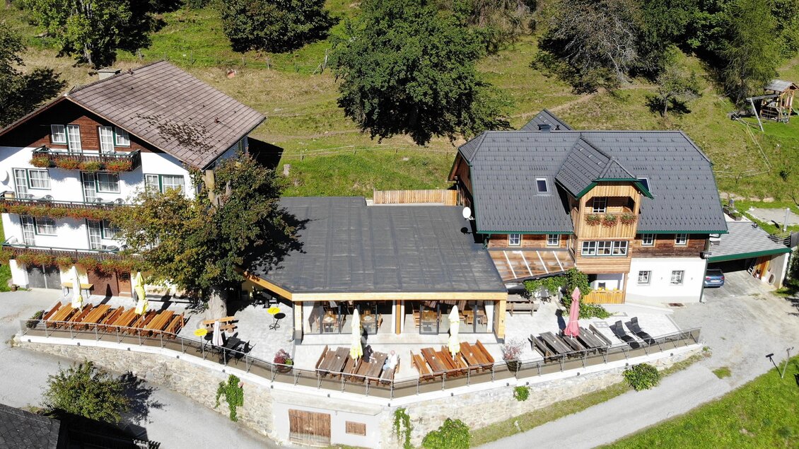 Ein gemütliches Gasthaus mit einer großen Terrasse und mehreren Sitzplätzen im Freien. Umgeben von grünen Wiesen und Bäumen. | © Gasthof Trattner