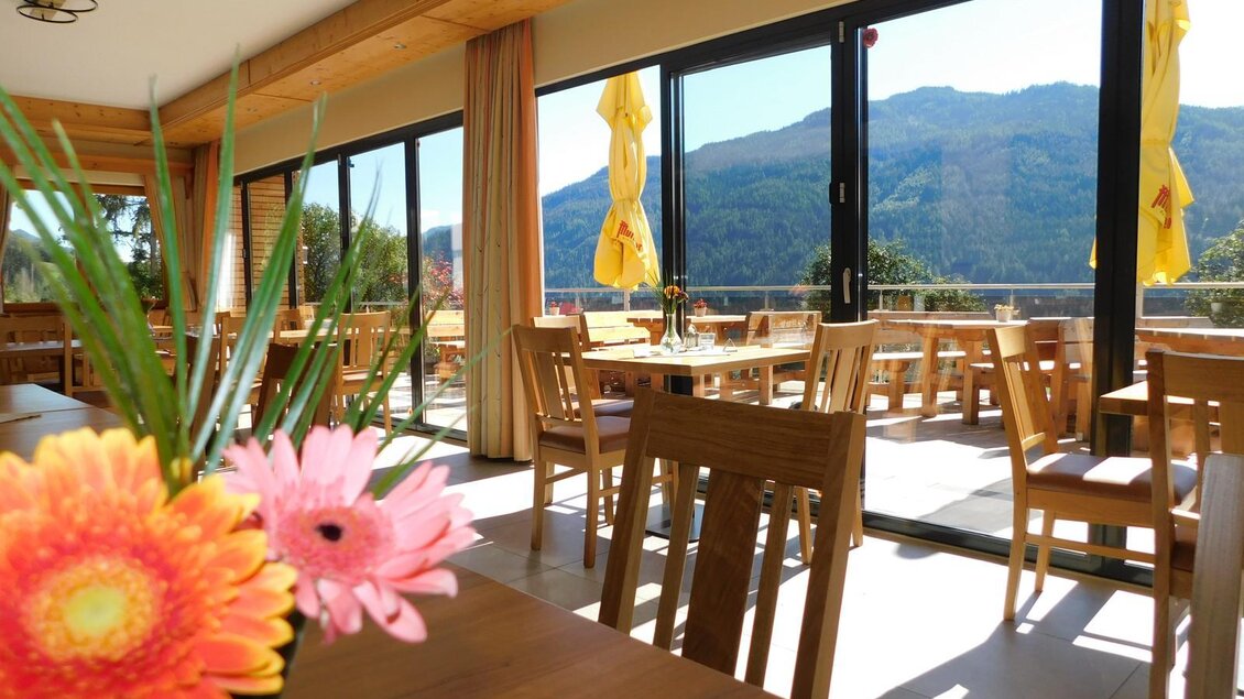 Ein helles Restaurant mit Holzstühlen und großen Fenstern. Im Hintergrund sind Berge und eine schöne Aussicht zu sehen. | © Gasthof Trattner