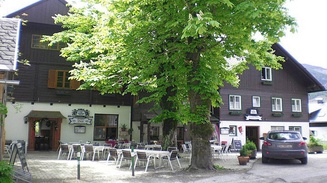 Ein traditionelles Gasthaus mit einem großen Baum im Vordergrund. Draußen stehen Tische und Stühle, ideal für Gäste im Freien. | © Gasthof Veit