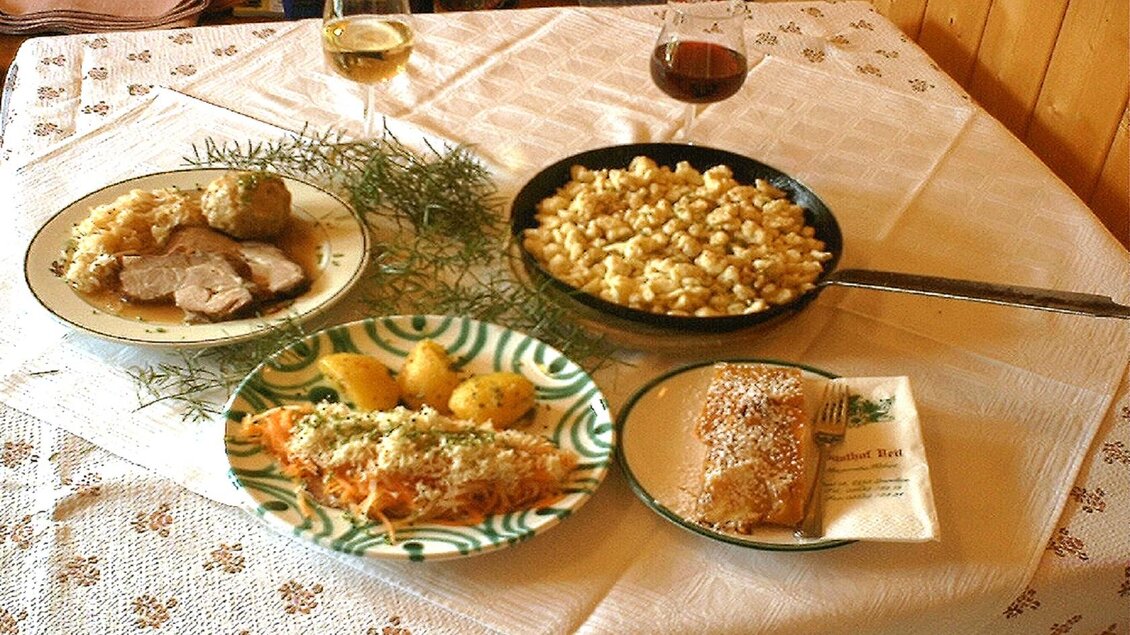 Ein festliches Essen mit verschiedenen Gerichten auf einem Tisch. Es gibt Fleisch, Beilagen, Pasta und ein Dessert sowie Wein. | © Steinegger