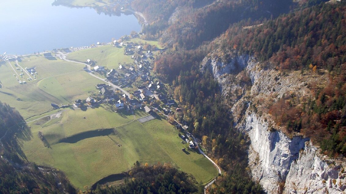 Eine malerische Landschaft mit einem kleinen Dorf am Ufer eines Sees. Saftige Wiesen und bewaldete Berge umgeben die ruhige Szenerie. | © Steinegger