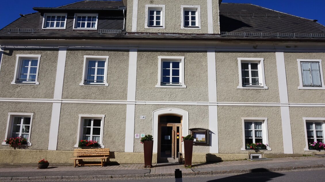 Ein großes, elegantes Gebäude mit hellen Wänden und einem Giebeldach. Vor dem Gebäude stehen Pflanzen und eine Holzbank. | © Tourismusverband Oststeiermark
