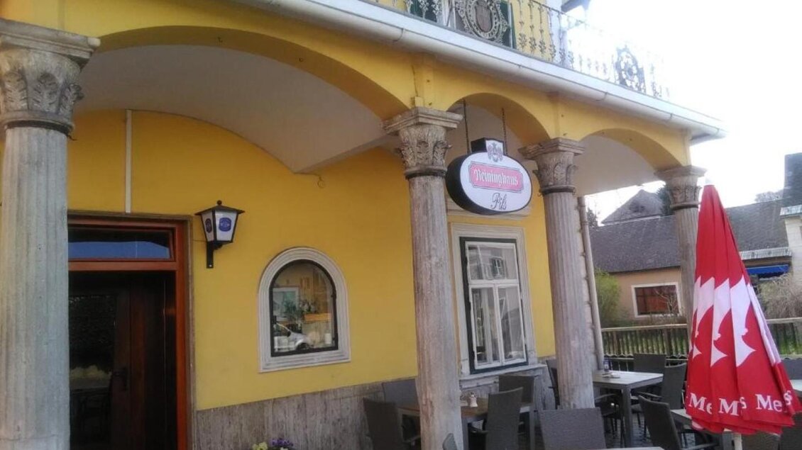 Ein gemütliches Restaurant mit gelber Fassade und Säulen. Vor dem Eingang stehen Tische und Stühle, daneben ein Sonnenschirm. | © Gasthof zur Goldenen Krone
