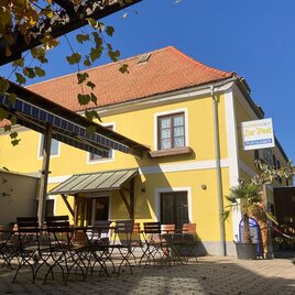 Gelber Gasthof Zur Post in Peggau mit Gastgarten, Tischen und Stühlen vor dem Gebäude unter blauem Himmel. | © Gasthof Zur Post