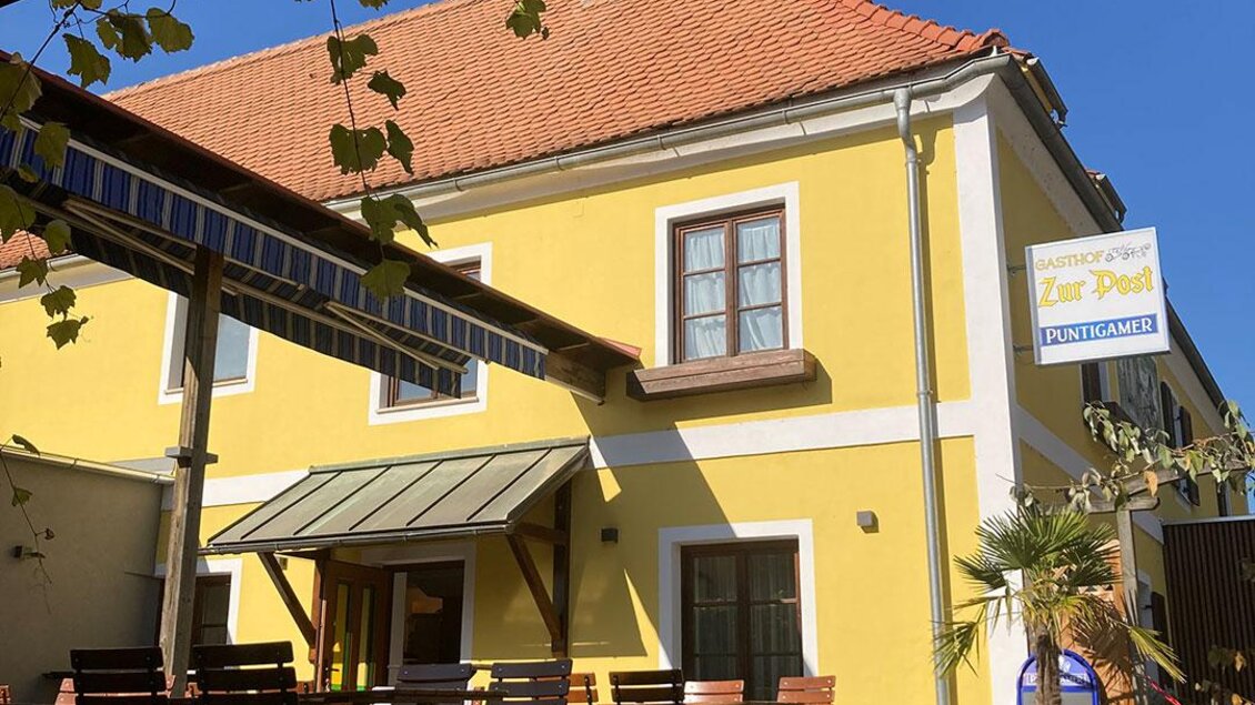 Gelber Gasthof Zur Post in Peggau mit Gastgarten, Tischen und Stühlen vor dem Gebäude unter blauem Himmel. | © Gasthof Zur Post