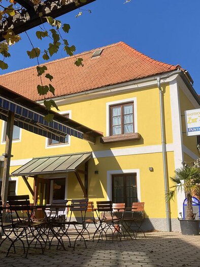 Yellow inn Zur Post in Peggau with a garden, tables, and chairs in front of the building under a blue sky. | © Gasthof Zur Post