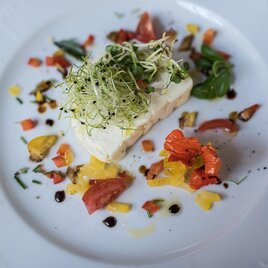 Ein elegantes Gericht bestehend aus einem Stück Fisch, garniert mit frischen Kräutern und buntem Gemüse. Die Präsentation ist ansprechend mit verschiedenen Farben und Texturen. | © Jean Van Luelik Photographer