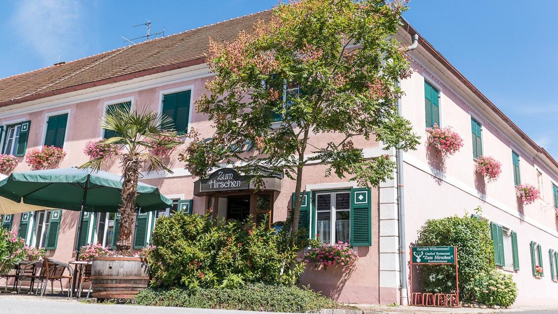 Ein charmantes Restaurant mit pinker Fassade und grünen Fensterläden. Umgeben von Pflanzen und einem gemütlichen Außenbereich. | © Jean Van Luelik Photographer
