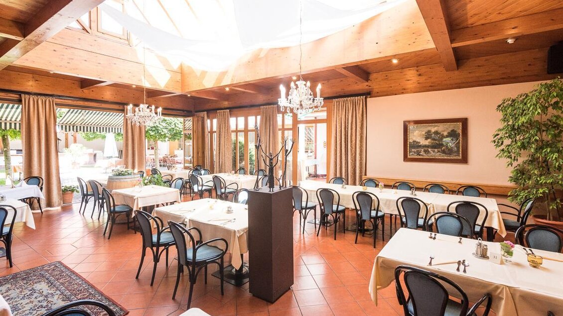 Ein einladender Restaurantbereich mit großen Fenstern und Holzelementen. Die Tische sind elegant gedeckt und mit Stühlen in klassischem Design ausgestattet. | © Jean Van Luelik Photographer