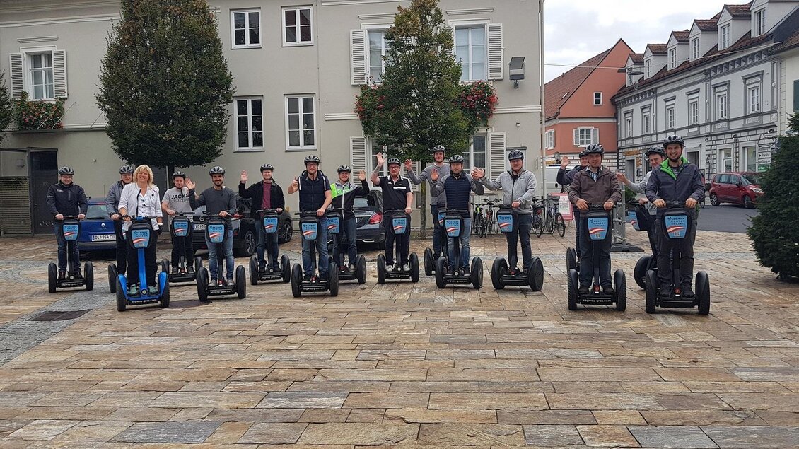 Eine Gruppe von Menschen steht auf Segways in einer städtischen Umgebung. Sie lächeln und winken in die Kamera. | © Claudia Dunst
