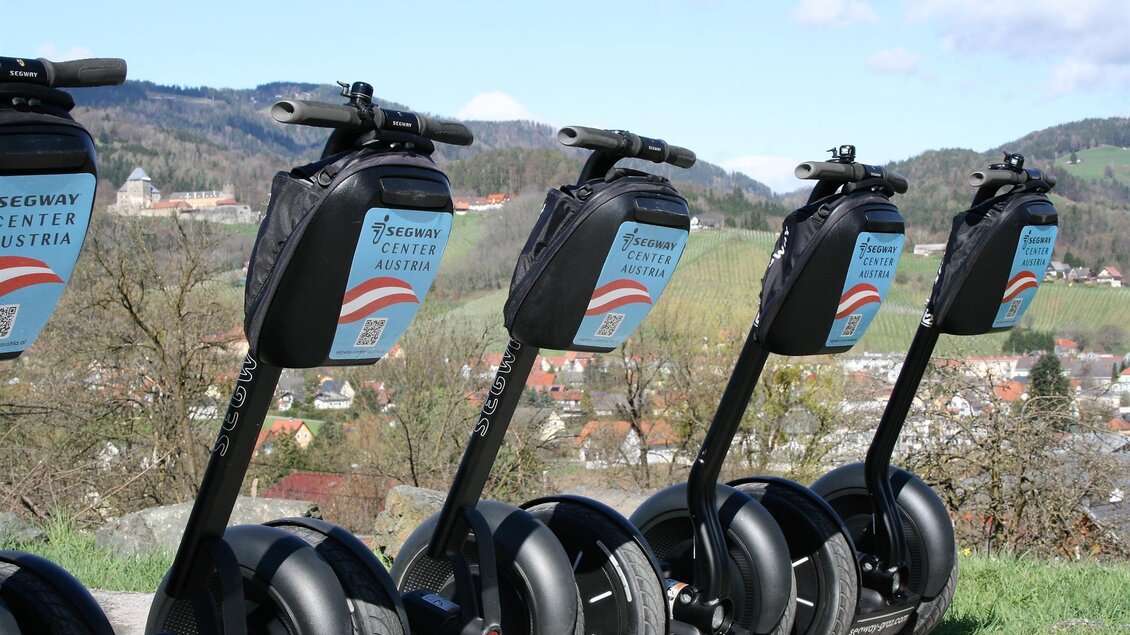 Mehrere Segways stehen in einer Reihe auf einem Weg. Im Hintergrund sind sanfte Hügel und ein klarer Himmel zu sehen. | © Claudia Dunst