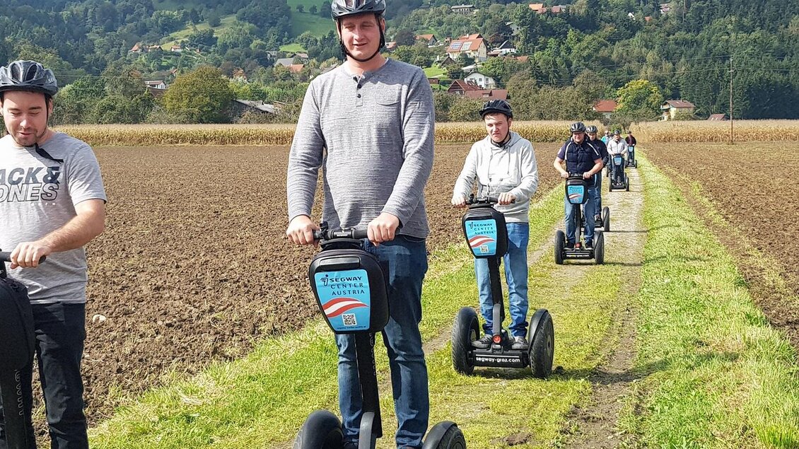 Eine Gruppe von Menschen fährt auf Segways durch ein Feld. Im Hintergrund sind Bäume und eine ländliche Landschaft zu sehen. | © Claudia Dunst