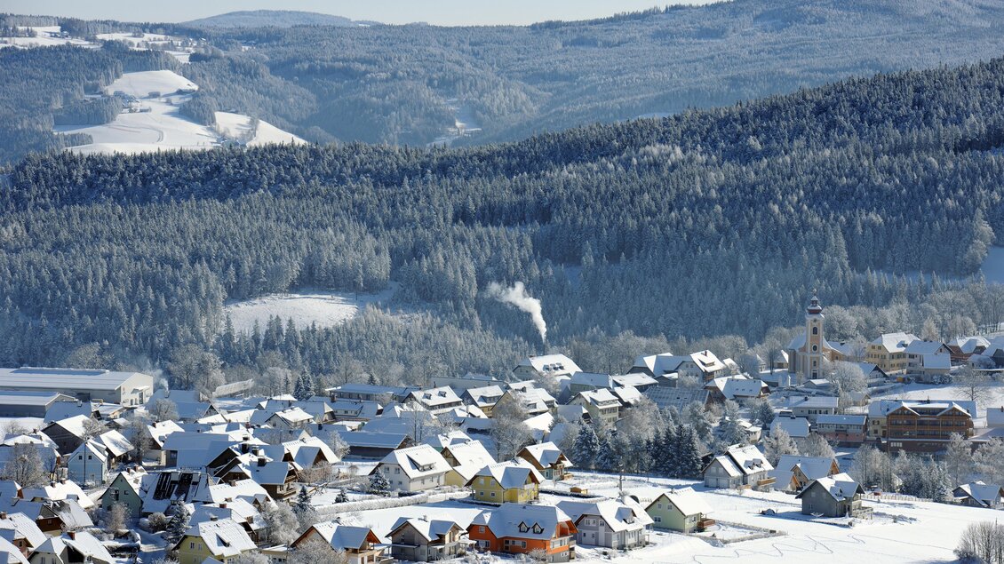 Eine winterliche Landschaft mit schneebedeckten Dächern und einem kleinen Dorf. Im Hintergrund sind Hügel und Wälder zu sehen. | © Gery Wolf