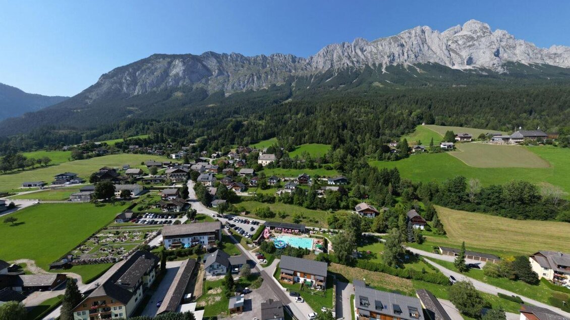 Luftaufnahme einer ländlichen Gemeinde mit Häusern, Wiesen und Poolanlage vor beeindruckender Bergkulisse: | © Gemeinde Mitterberg-Sankt Martin