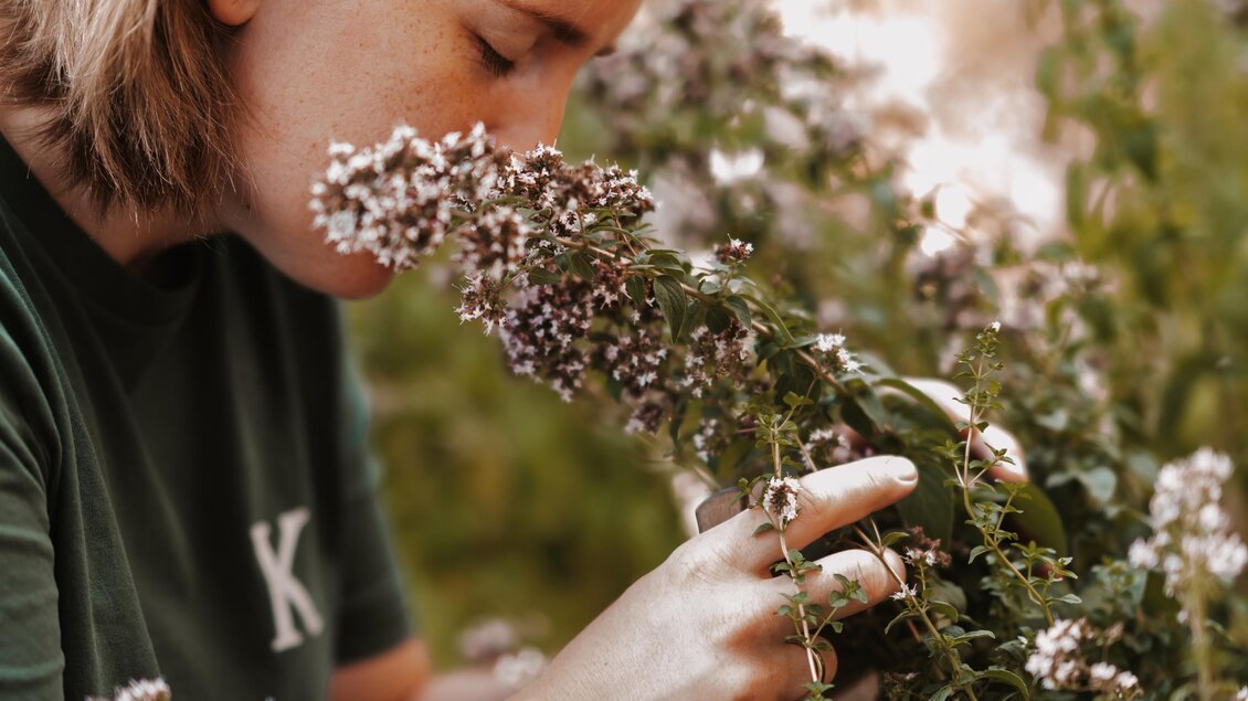 Eine Person riecht an Blumen in einem Garten. Die Atmosphäre ist ruhig und blumig. | © Genuss-Geschwister Kästenburg