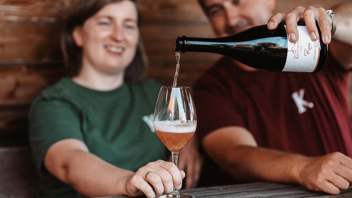Zwei Personen stehen an einem Tisch und schenken ein Getränk in ein Glas ein. Die Atmosphäre ist entspannt und gesellig. | © Genuss-Geschwister Kästenburg