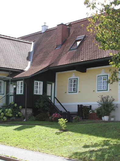 Ein charmantes Haus mit gelber Fassade und einem roten Dach. Der Garten ist grün und einladend, mit einigen Blumen und Pflanzen. | © Renate Jöbstl