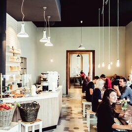 Ein modernes Café mit einem hellen Innenraum. Gäste sitzen an Tischen und genießen Getränke und Speisen. | © Ginko - Lupi Spuma