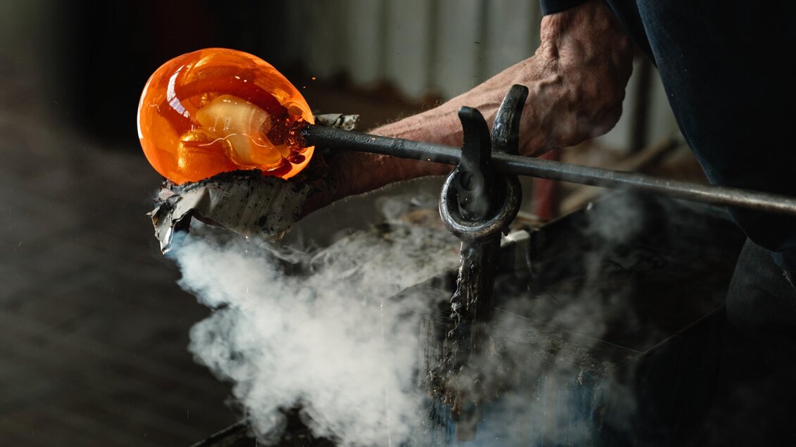 Orange glühendes, flüssiges Glas an einer Glasmacherpfeife wird für das Glasblasen vorbereitet. | © Bernd Grosseck