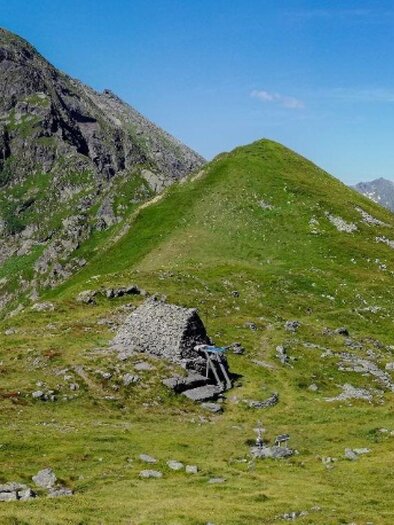A vast mountain landscape with green meadows and tall peaks. The sky is clear and blue, ideal for hiking in nature. | © Roland Gutwenger