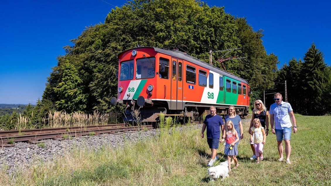 Unterwegs in der Natur – während die Gleichenberger Bahn ruhig vorbeigleitet, genießt eine Familie den Spaziergang durch die sanften Hügel. Ein Zusammenspiel aus Bewegung, Entschleunigung und gemeinsamen Momenten, das die Erlebnisregion Thermen- & Vulkanland im Südosten der Steiermark so besonders macht. | © StB