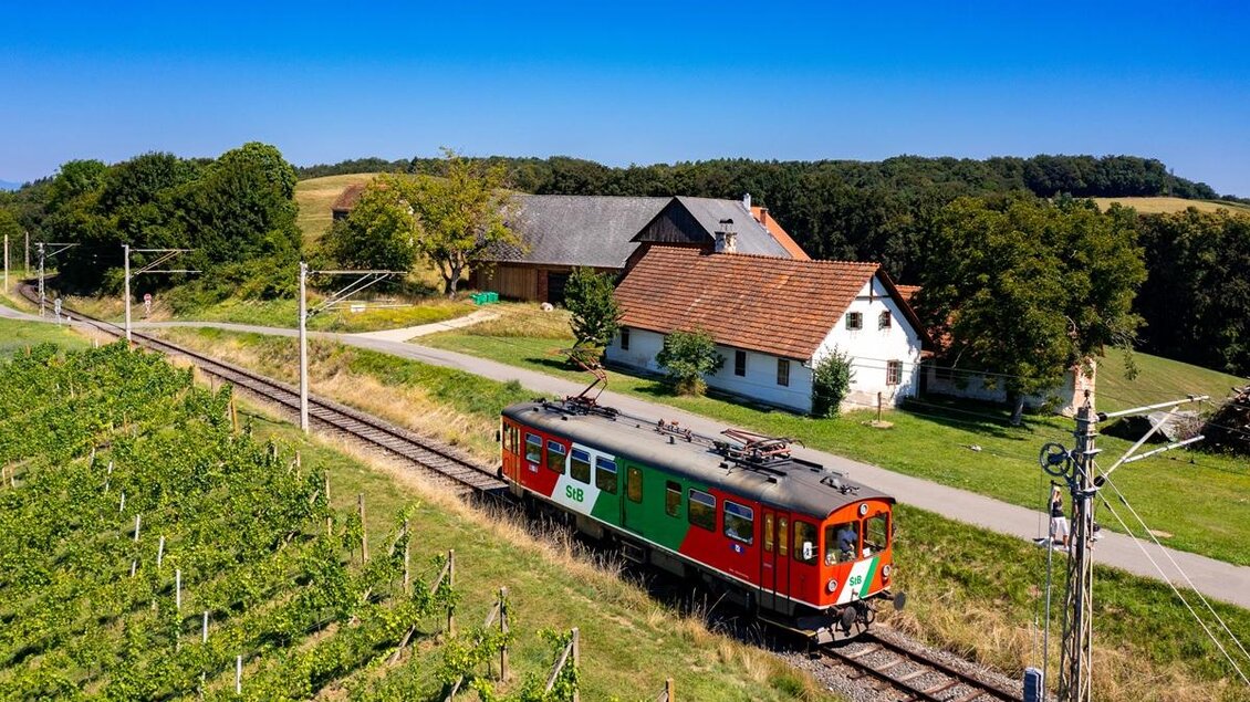 Sanft gleitet die Gleichenberger Bahn durch die sonnenverwöhnten Weinberge – vorbei an idyllischen Höfen, eingebettet in die weichen Hügel der Südoststeiermark. Ein Moment zum Durchatmen, zum Staunen, zum Ankommen. So fühlt sich entschleunigtes Reisen in der Erlebnisregion Thermen- & Vulkanland an – einfach zu schön, um nicht da zu sein. | © StB