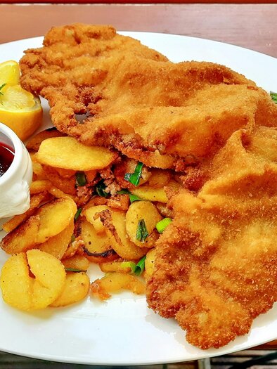 Ein Teller mit paniertem Fisch, serviert mit Bratkartoffeln und einem kleinen Dip aus Preiselbeeren. Daneben liegt ein Stück Zitrone zur Garnierung. | © mark-konig-unsplash