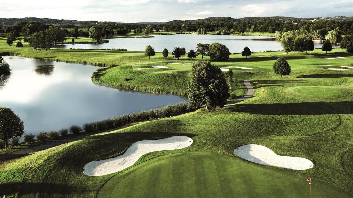 Eine weitläufige Golfanlage mit grünen Fairways und Sandbunkern. Im Hintergrund sind Seen und Bäume zu sehen. | © GV Murstätten